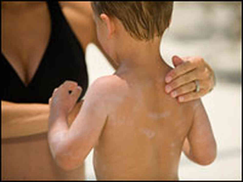 A woman applies sunscreen to her son's back.