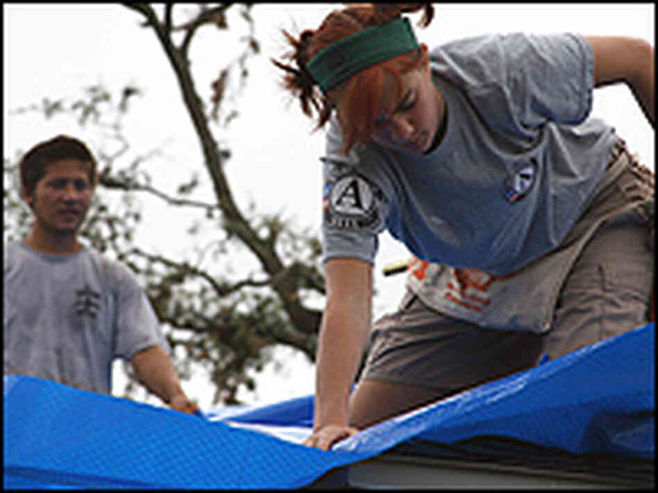 A young woman securing a blue tarp to protect a home. A young woman securing a blue tarp to protect a home.