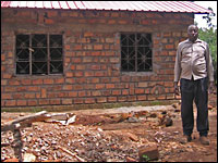 Enoch Obiero stands in front of the house he is rebuilding. In May, a mob burned the previous house to ashes. His wife, who was killed in the attack, is buried nearby.