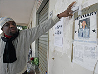 A man points to a poster showing a portrait of Karim Yabuku.