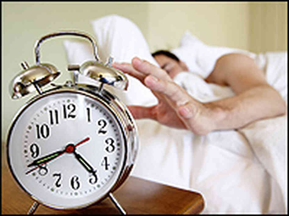 A man reaches to snooze his alarm clock. A man reaches to snooze his alarm clock.
