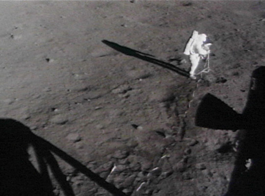 Astronauts move the lunar camera onto a tripod on the moon.