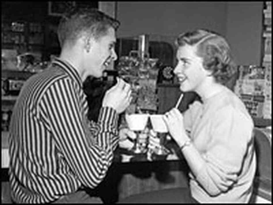 A young man and woman have drinks at the soda fountain on a date.