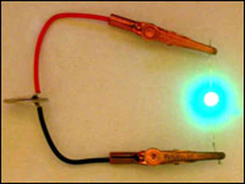 A small battery with electrodes built from viruse powers an LED light. A small battery with electrodes built from viruse powers an LED light.