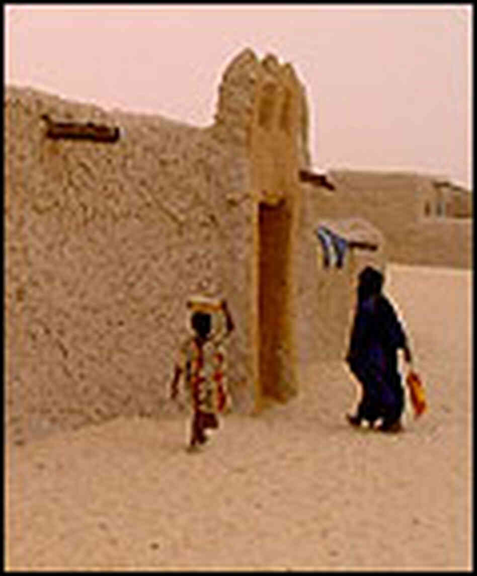 People walk past earthen walls, as sand clouds the desert skies. People walk past earthen walls, as sand clouds the desert skies.
