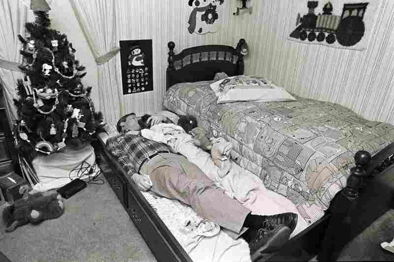 In Morgan's trundle bed, John consoles his son, who's distraught because David refused to let him be part of his birthday slumber party. January 1986.