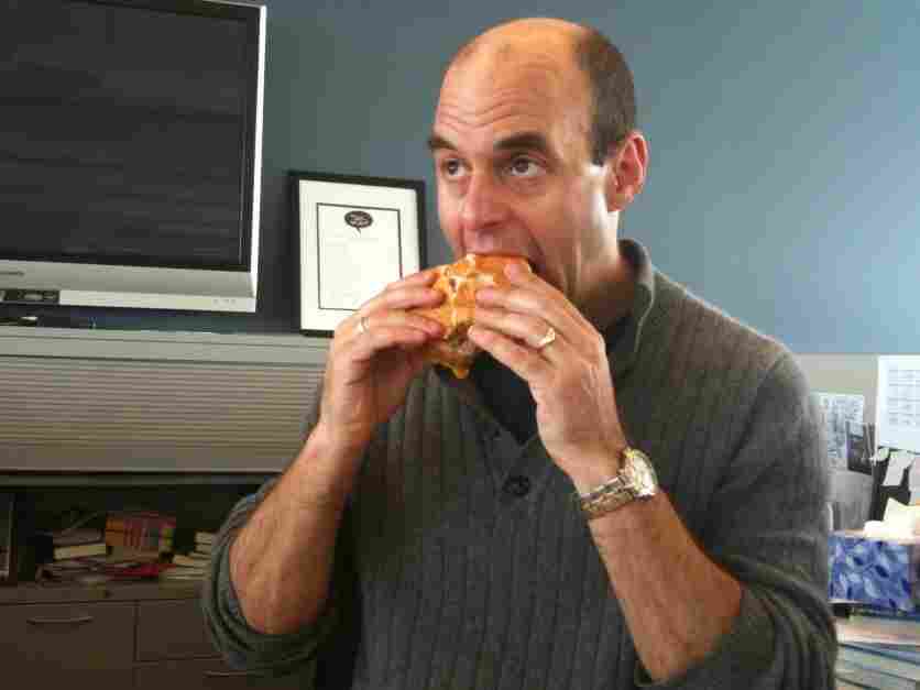 Peter Sagal bites a sandwich.
