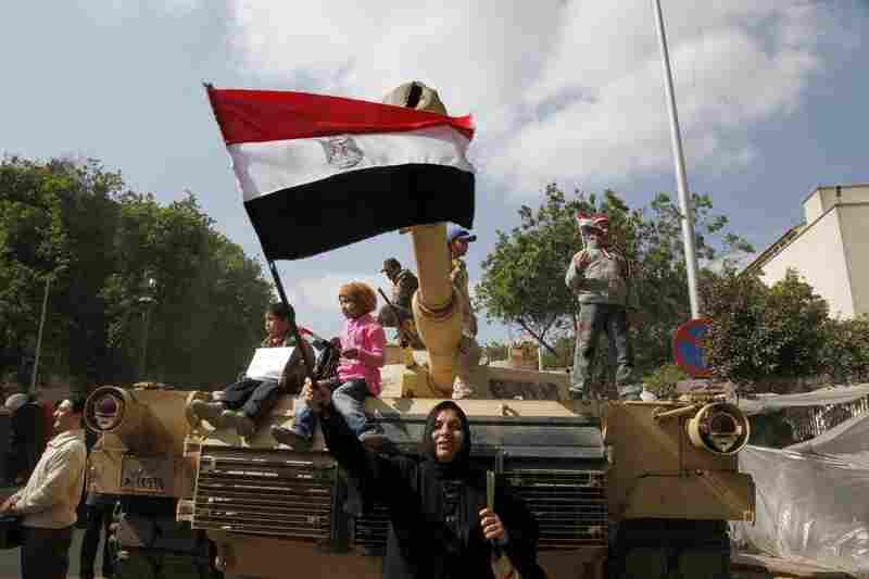 An Egyptian woman waves the national flag in front of a tank. 