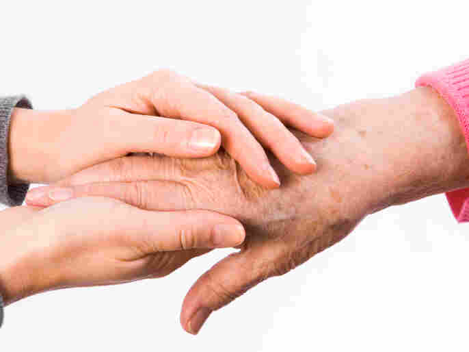 A young woman holds an older woman's hand.