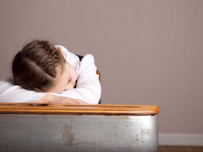 A sleepy girl snoozes at her school desk.