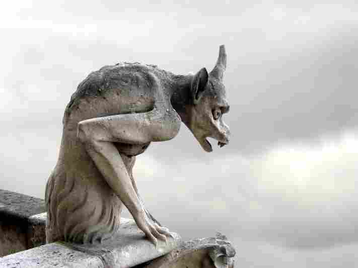 A creepy gargoyle looks onto an overcast sky.
