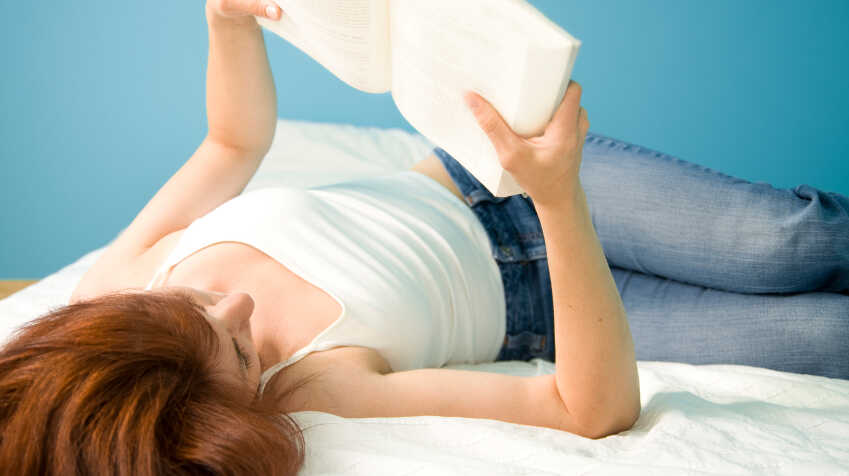 A girl lies on her back reading a book.