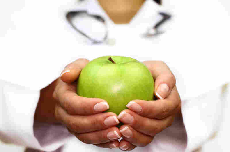 A female doctor holds an apple in her hands.