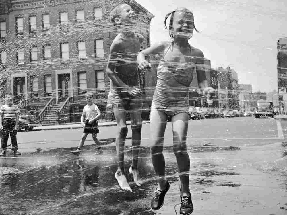 Two children jumping through a water hydrant's shower on a New York street. They have come from a neighbouring co-educational playgroup organised by the city's Police Department. (Photo by Orlando/Getty Images)