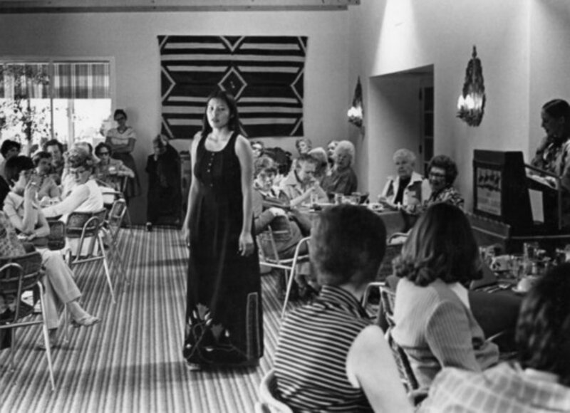 This photograph is from a 1977 fashion show by students in the Traditional Techniques course at the Institute of American Indian Arts. The dress that the girl is wearing is a modern adaptation inspired by woodlands Indian floral beadwork. 