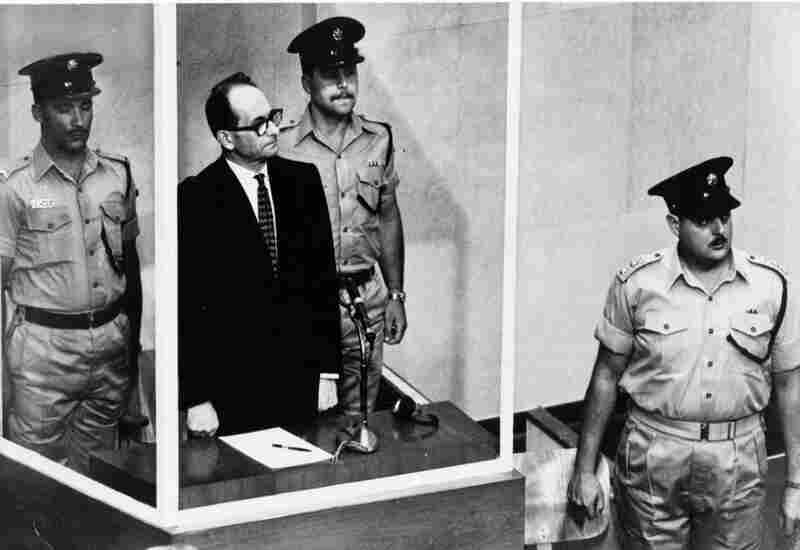 Adolf Eichmann stands in a bulletproof glass cage, flanked by guards, during his 1961 Nazi war crimes trial in Jerusalem. He was convicted of helping to exterminate Jews during World War II and sentenced to death. 