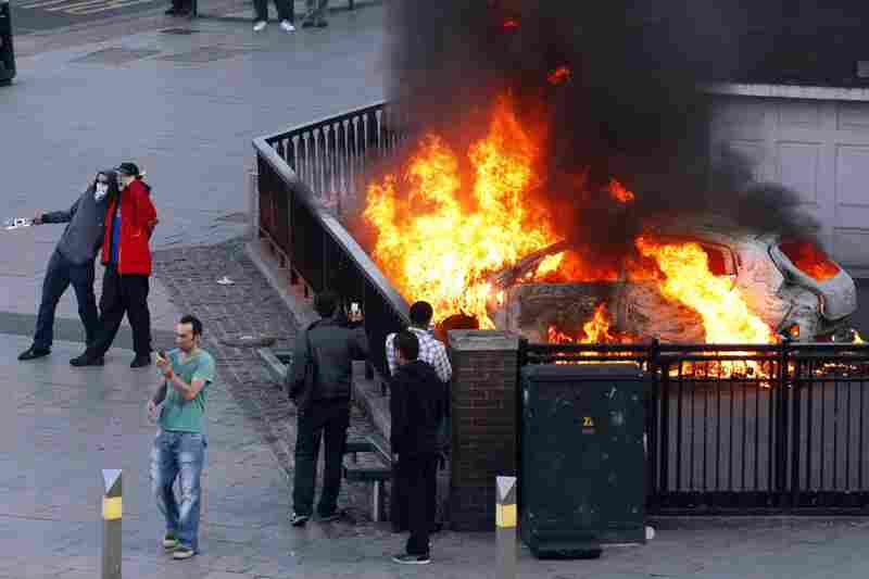 People pose for photos in front of a burning car set alight during the second night of civil disturbances in central Birmingham on Aug. 9. 