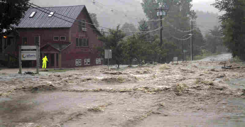 A person checks a building for occupants as raging floodwaters cross Route 100, closing the main road in Waitsfield, Vt., on Sunday. 