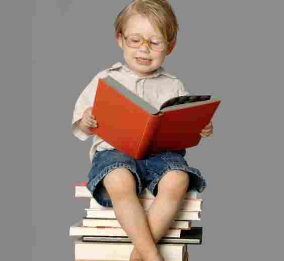 A boy reads, sitting on a stack of books.