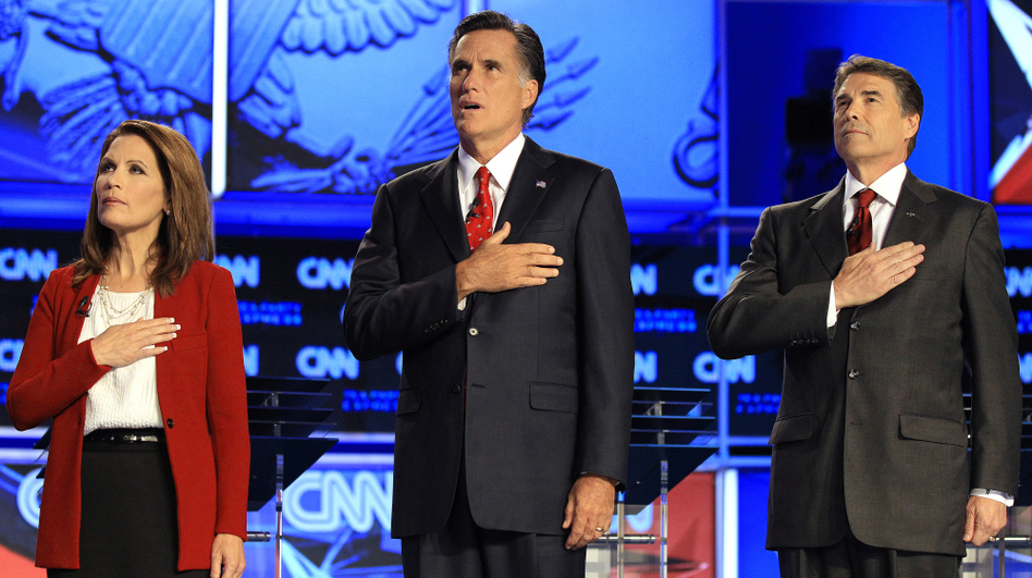 Republican presidential candidates (from left) Rep. Michele Bachmann, former Massachusetts Gov. Mitt Romney and Texas Gov. Rick Perry cover their hearts during the playing of the national anthem before a Republican presidential debate on Sept. 12. (Chris O'Meara/AP)