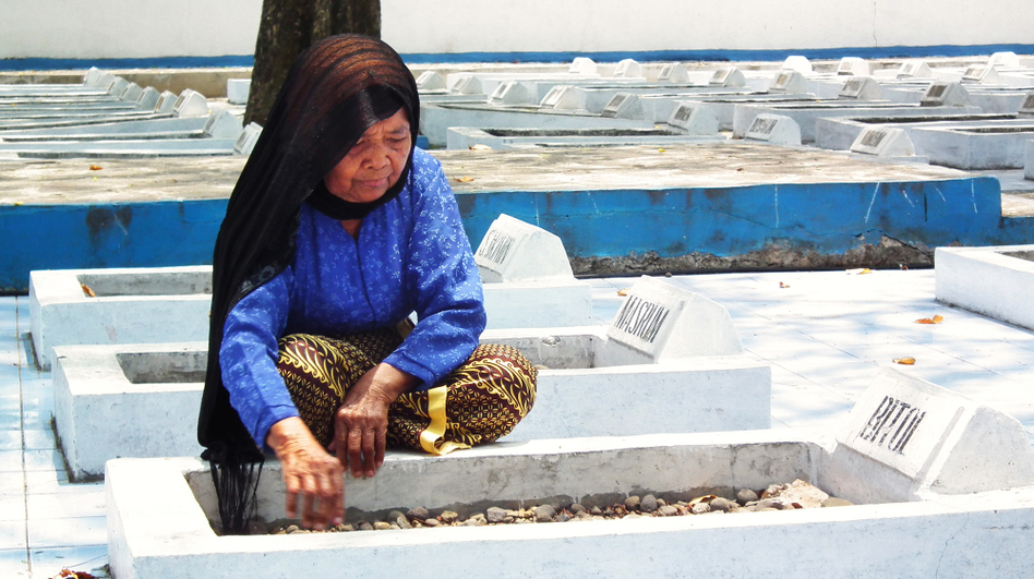 <p>Cawi Binti Baisan, 84, squats beside the grave of her first husband, Bitol, a farmer who was executed by Dutch soldiers in 1947. She is one of seven remaining widows of the more than 400 estimated massacre victims. A Dutch court recently ruled that the Dutch government must compensate the widows for their losses.</p> (Yosef Riadi for NPR)