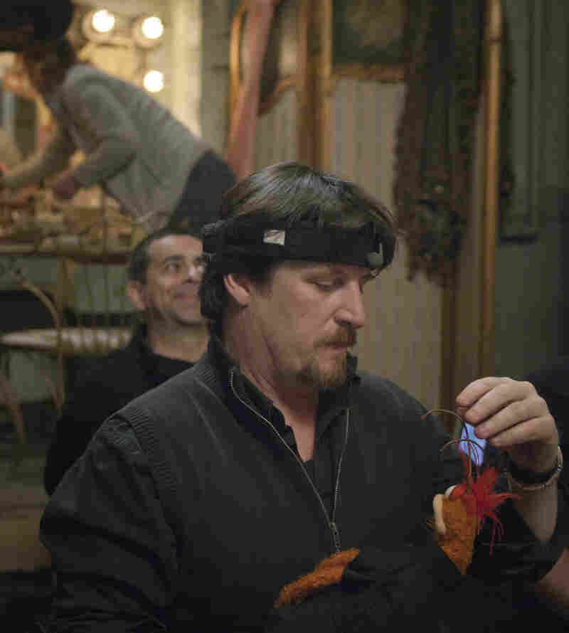 Muppet wrangler Bill Barretta — wired for sound with a headband microphone — adjusts one of Pepe the Prawn's antennae.