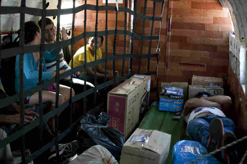 A passenger rests on top of cargo while others talk to each other during a flight.