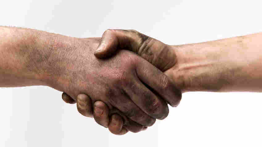 Two people with dirty hands shaking hands.