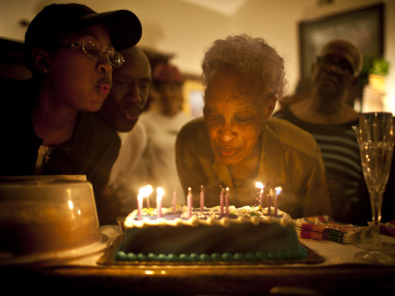 Ida Christian, who suffers from dementia, gets help from her granddaughter, Yolanda Hunter (left), in blowing out the candles on her birthday cake. Yolanda quit her lucrative job to become Ida's full-time caregiver. (Kainaz Amaria/NPR)