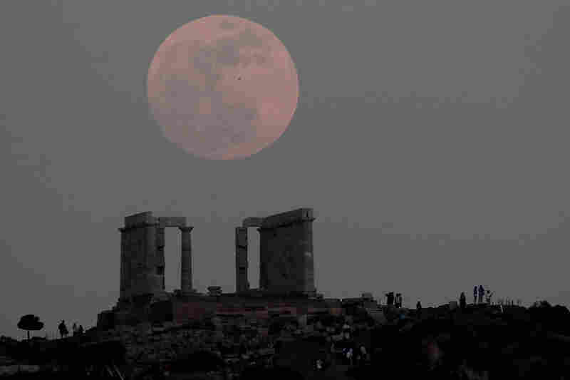 Tourists look at the moon rising over the ancient temple of Poseidon at cape Sounion, south of Athens. 
