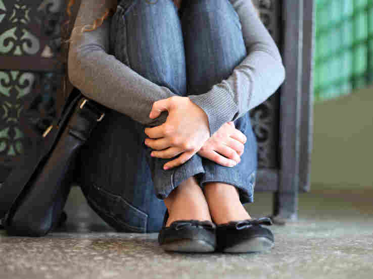 A teenage girl sits on the floor with her hands crossed over her legs.