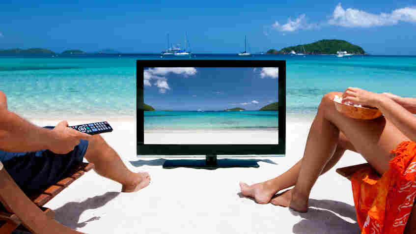 Two people watching TV at the beach.