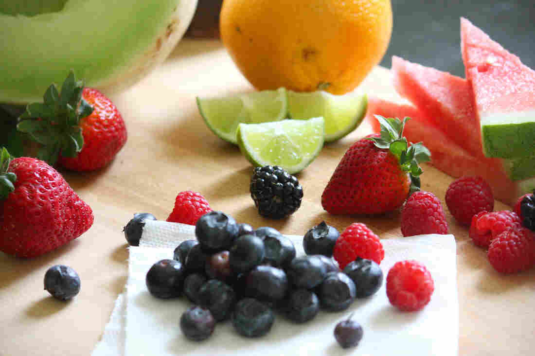 Fruit salad ingredients, including honeydew, watermelon, orange, lime, strawberries, blueberries and raspberries.