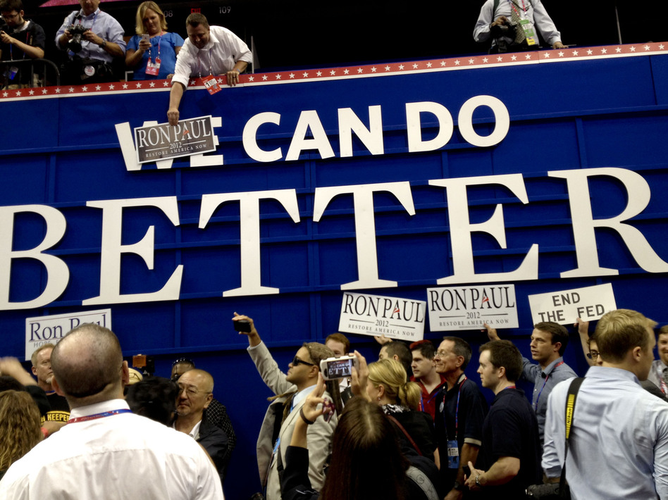 Ron Paul supporters pose with posters on the floor of the RNC on Monday in Tampa. They put "Ron Paul" over the word "We" on a GOP sign that says "We Can Do Better." (Liz Halloran/NPR)
