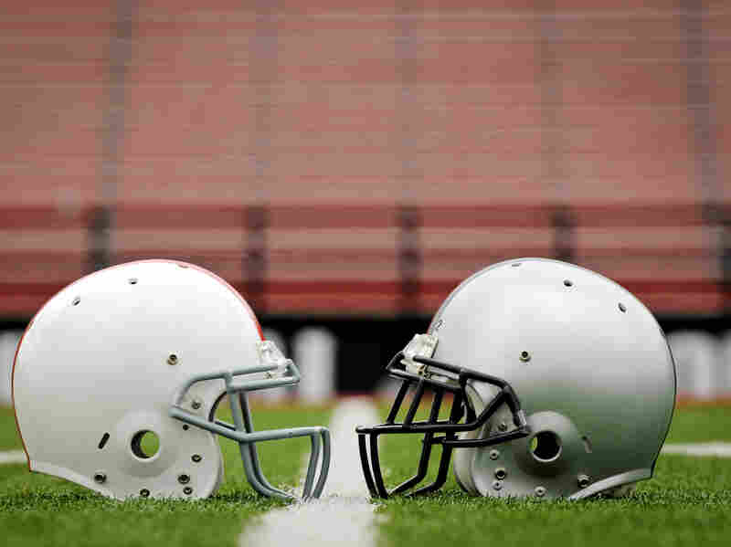 Two football helmets face each other on a field.