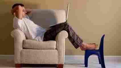 Man sitting on a club chair reading from his laptop.