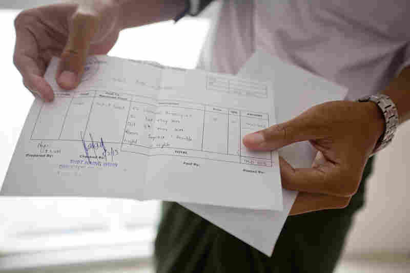 One of Aung's employees holds up the receipt of a payment he is about to deliver to one of Aung's partner hotels. Even though Aung enables tourists to handle their travel bookings online, he still has to deliver cash to his partners by hand.