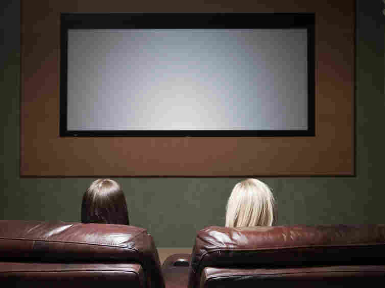 Two women watch a movie screen.