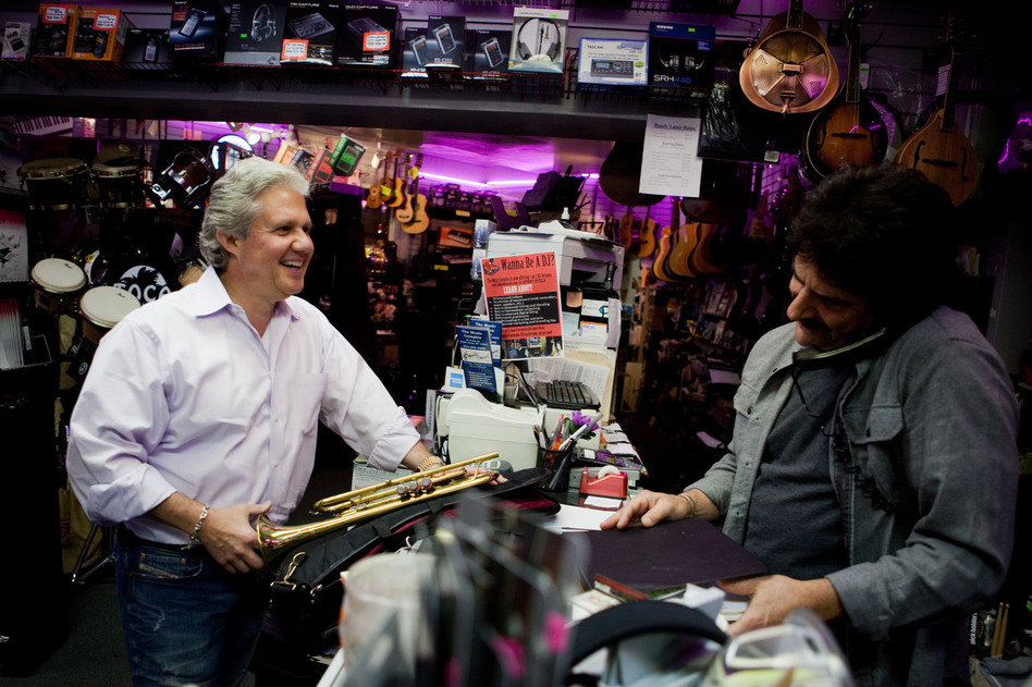 Michael Pagliaro, left, laughs with Paul Scattaretico at the Muzic Store Inc. in Dobbs Ferry, N.Y., as Pagliaro picks up instruments for his rental business. Before Pagliaro had a hip replacement, pain made it difficult to work. (Maggie Starbard/NPR)