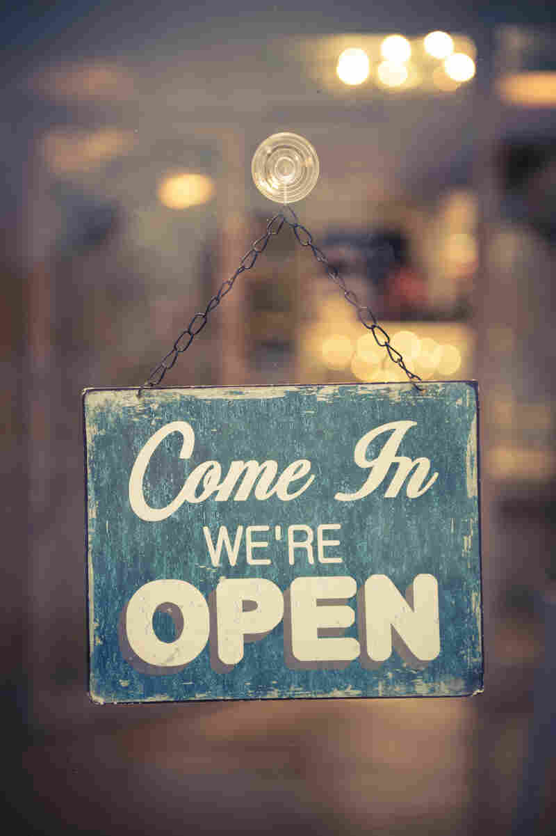 A weathered sign hanging in a store window says, "Come in; we're open."