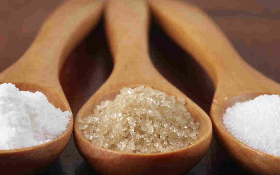 Three wooden spoons with different kinds of sugar in each.