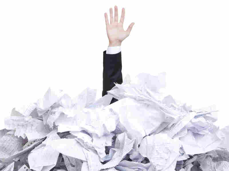 A man's arm sticks straight out of a pile of crumples papers.