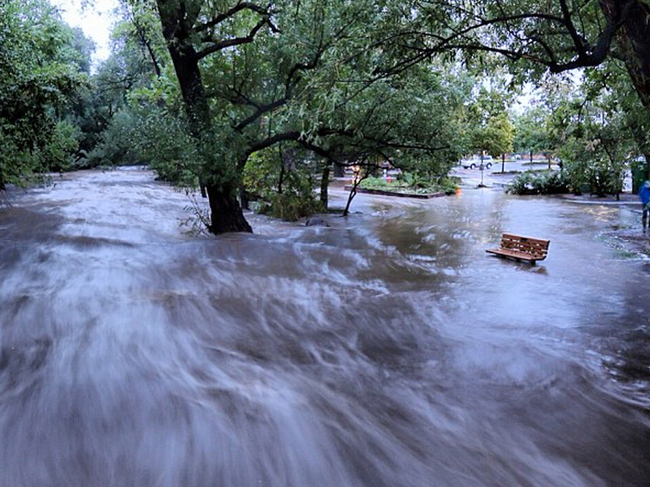 In this image made with a slow shutter speed which blurred the rushing water, flood waters course through a small park in Boulder, Colo., on Thursday.