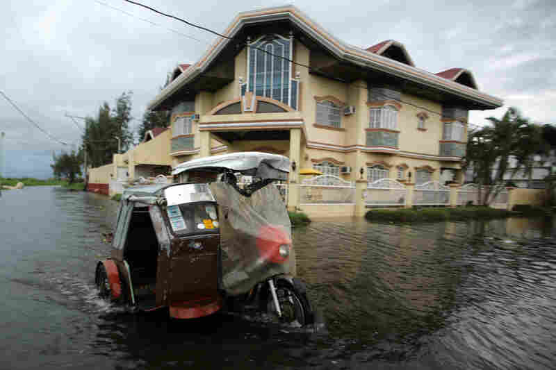 A three-wheel motorcycle maneuvers in floodwaters in Taguig City. Haiyan, the most powerful cyclone in decades, has killed at least four people, according to The Associated Press.