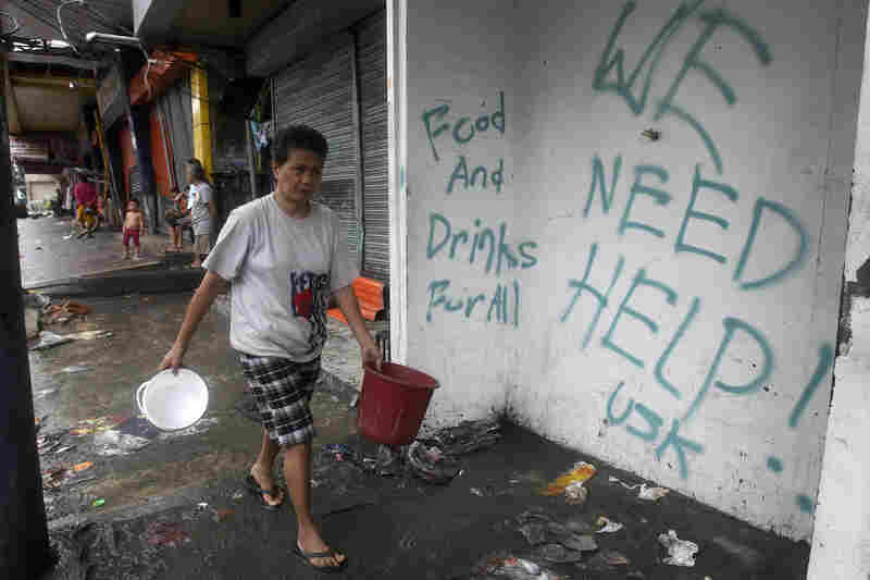 A resident walks past a wall with a graffiti calling for help in Tacloban. Rescue workers tried to reach towns and villages in the central Philippines on Tuesday that were cut off by the powerful typhoon.