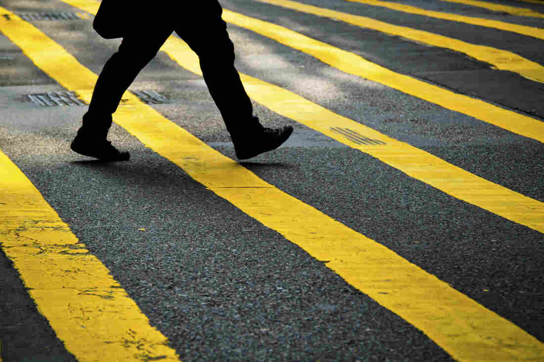 The lower-half of a person walking across a yellow-striped crosswalk in the city.
