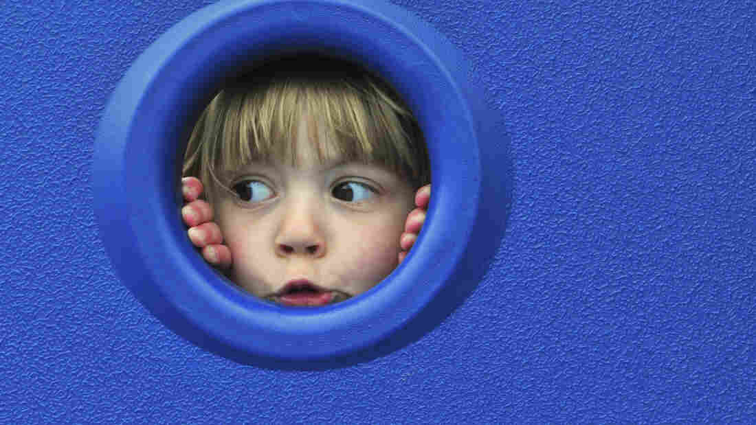 A child looks through a round opening in a blue wall.