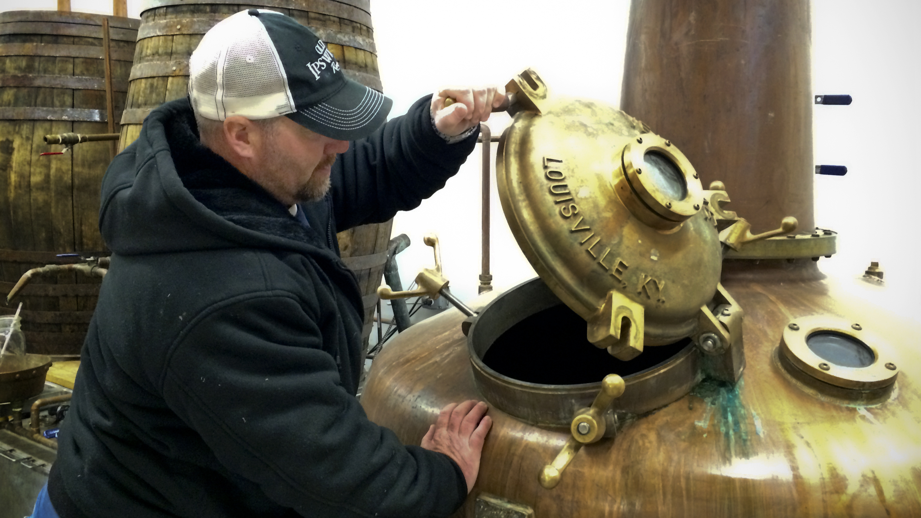 Evan Parker of Turkey Shore Distilleries lifts the distilling kettle's brass door. Parker climbs down this hole between batches to clean the kettle and says he had to measure his hips at first to make sure he'd fit through. (NPR)