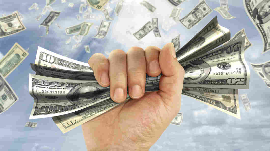 A hand grabs a wad of money against a background of money falling from the sky.