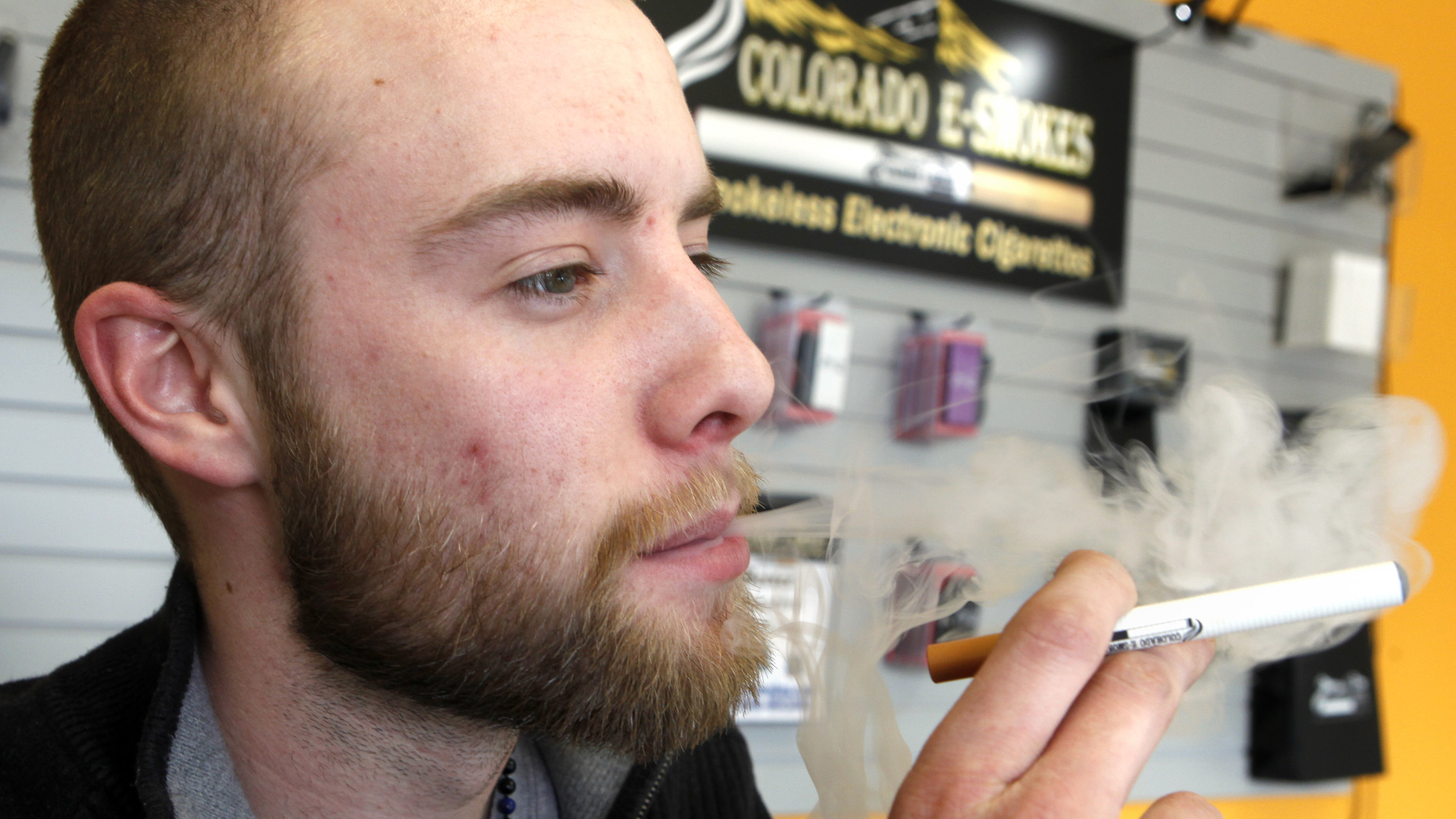 Blair Roberts, a 22-year-old sales associate at Colorado E-Smokes, "vapes" with an electronic cigarette in the Aurora, Colo., store. In the absence of federal rules, Colorado is among states that considered its own age requirements for the nicotine-delivery devices.